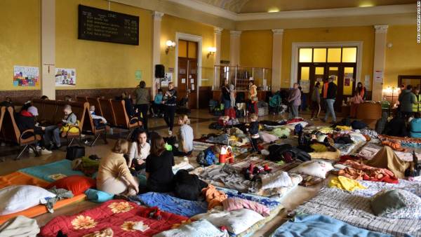 Women and children rest on wooden benches and mattresses in a room above Lviv train station